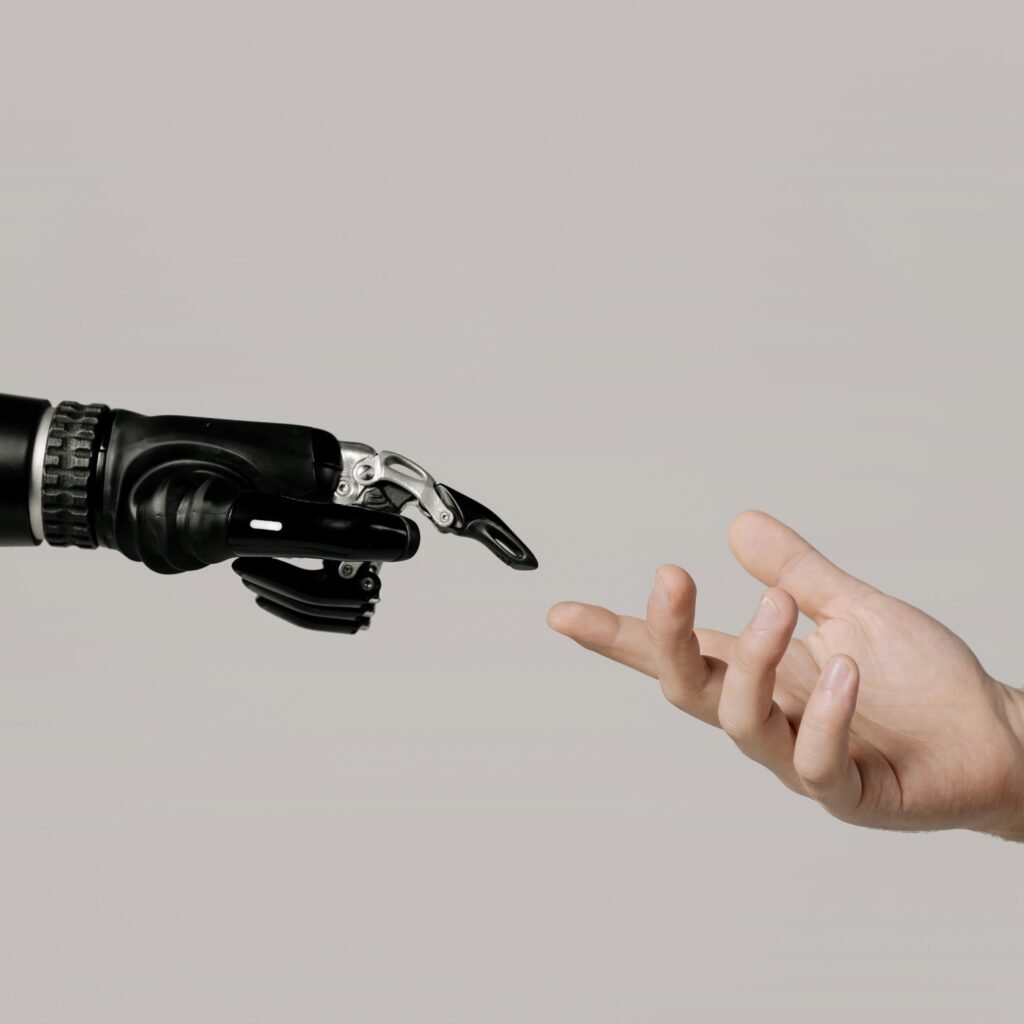 pexels photo 6153343 6153343 A human hand reaching to touch a bionic prosthetic hand on a white background.