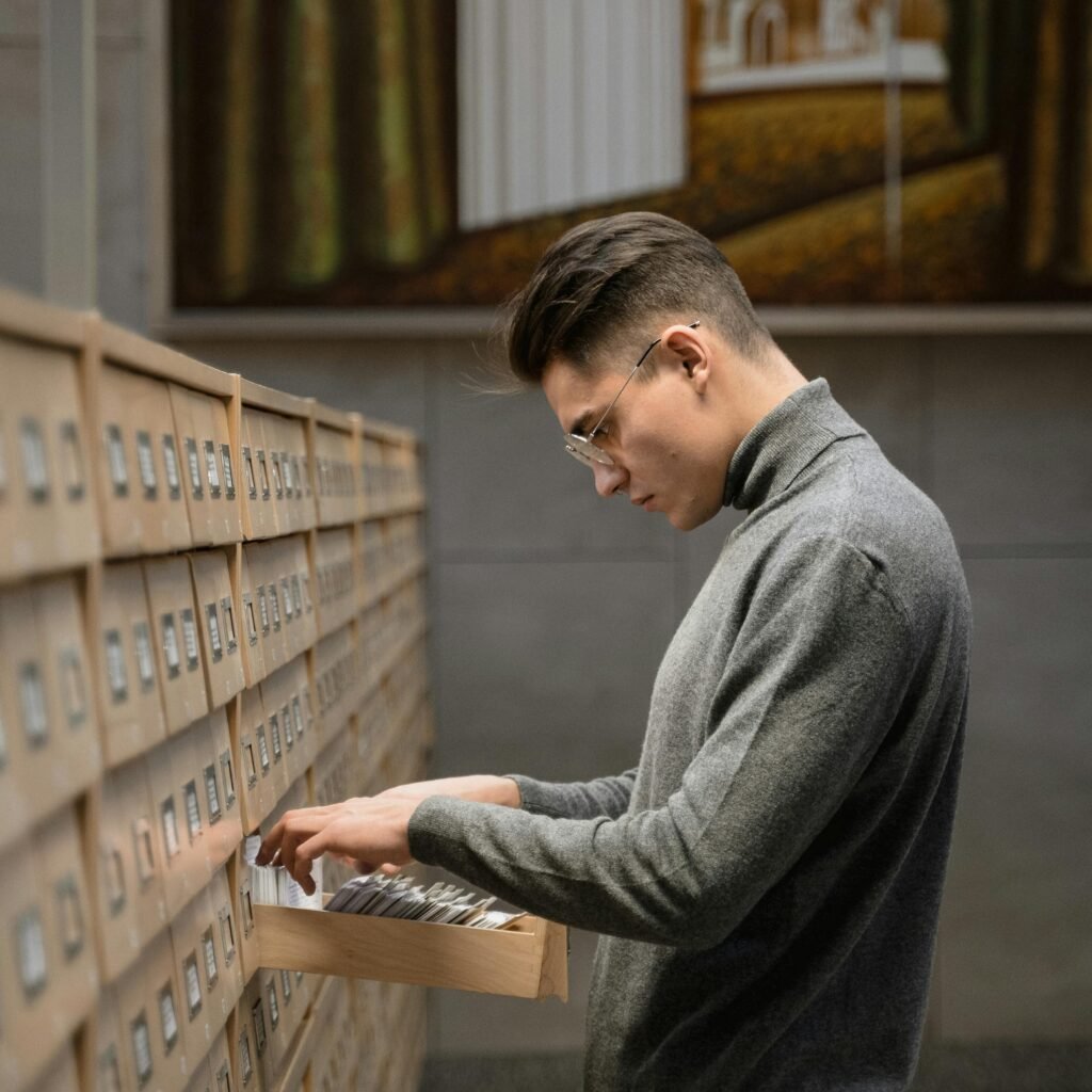 pexels photo 6550172 6550172 A man stands in a library looking through card files from a drawer, surrounded by bookshelves.
